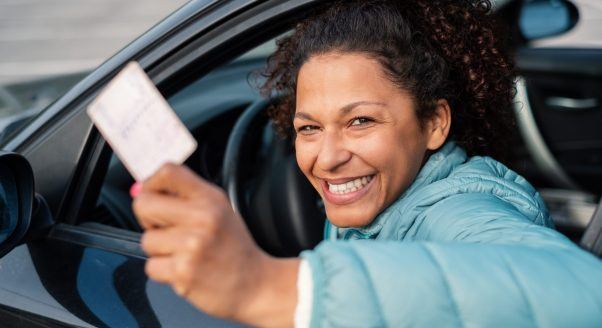 woman in car holding license and smiling