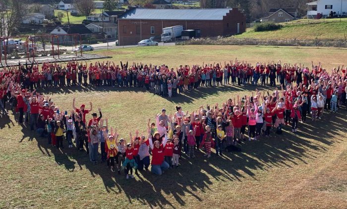 children and teachers form a heart shape in a field outside school