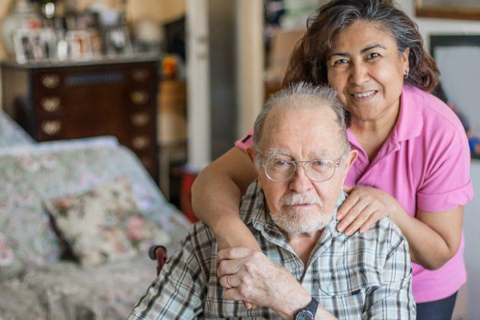 hispanic woman embraces older white man in home setting