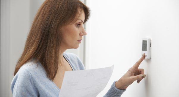 woman holding heating bill, adjusting thermostat