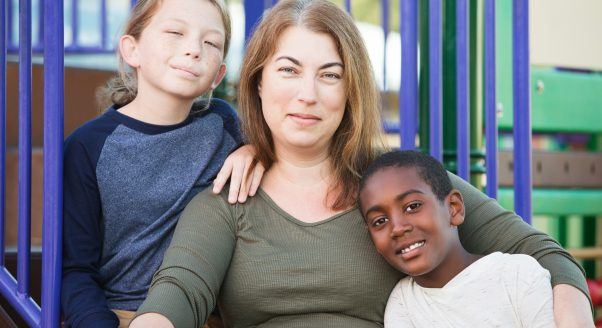 middle aged white woman hugs two children of different races at a prark