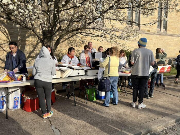 Legal Aid of West Virginia's Clarksburg office staff serve dinner to members of the community at a long row of tables.