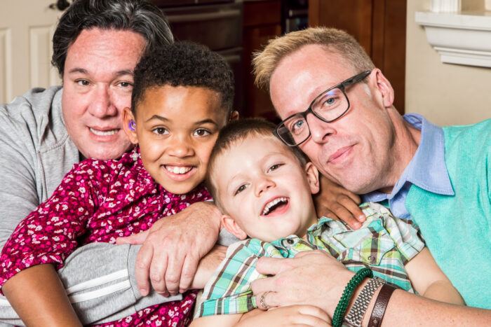 an interracial family poses: two men with their two sons smiling and embracing
