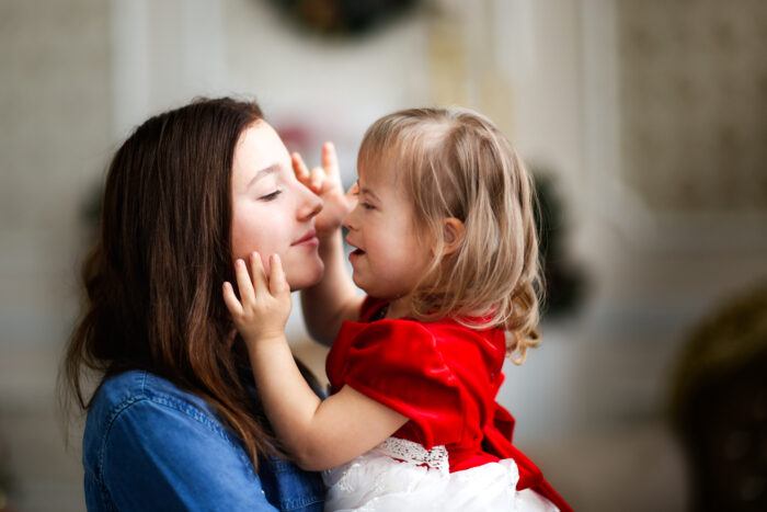 woman holds smiling child with Down Syndrome, they look at each other with happy expressions