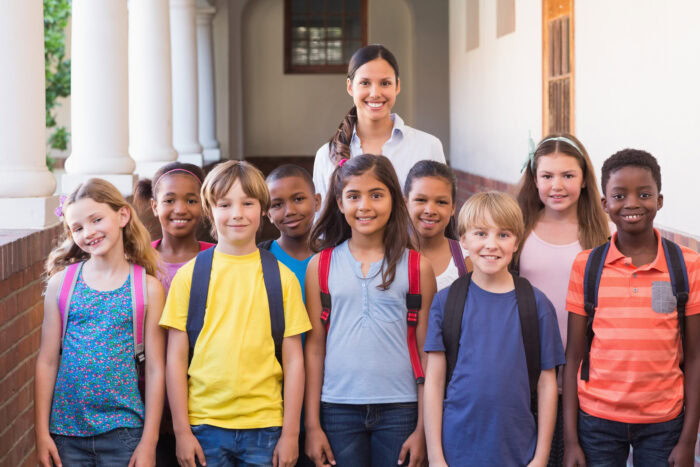 group of diverse elementary school kids stand in hallway with their teacher