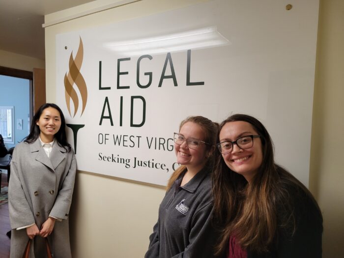 Three Vanderbilt law students pose in front of legal aid logo