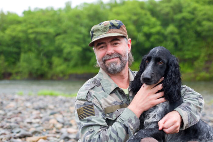 man in military fatigues with dog smiles at camera