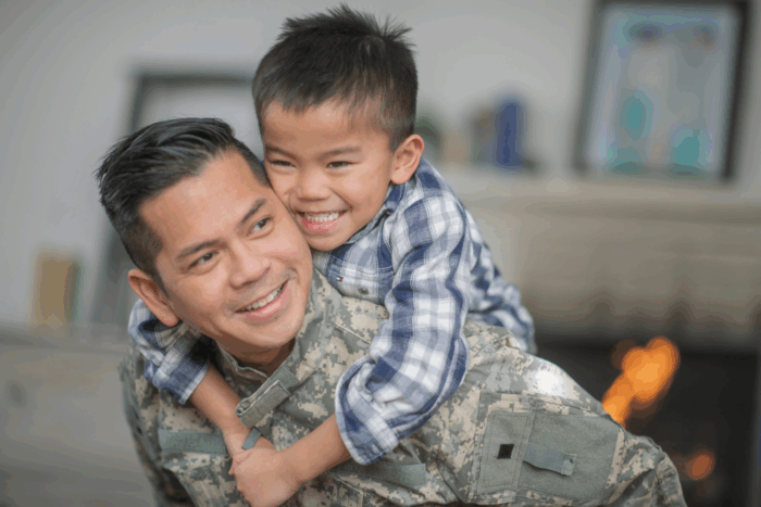 Father in military fatigues carries son on back, smiling
