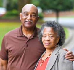 Older couple stands together with man's arm around woman.