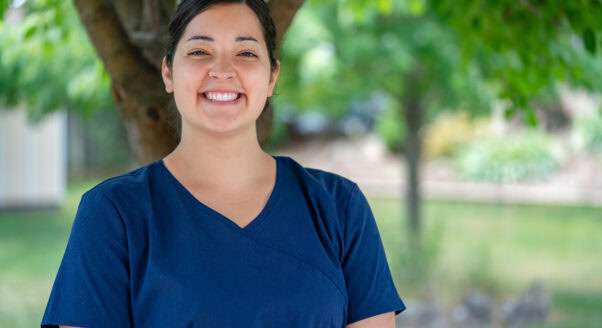 Nurse in scrubs smiles at camera while she stands outside.