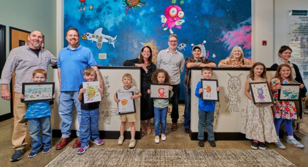 Artists stand in front of the PlaySpace mural in Legal Aid's Charleston office lobby