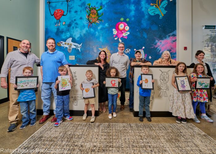 Artists stand in front of the PlaySpace mural in Legal Aid's Charleston office lobby