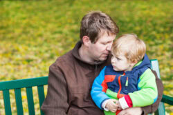 man sits on bench holding young son