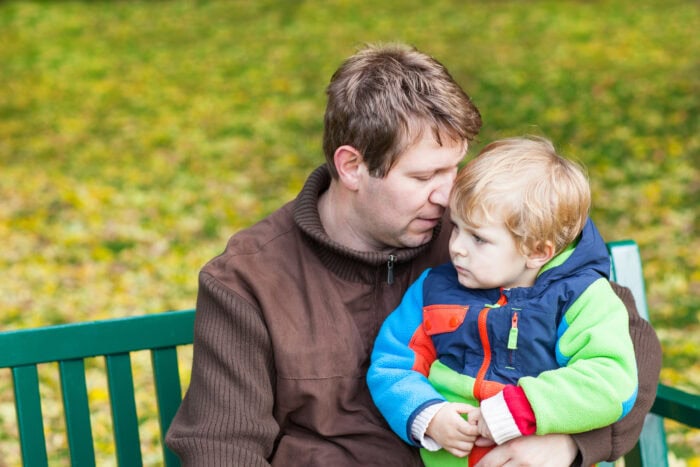 man sits on bench holding young son