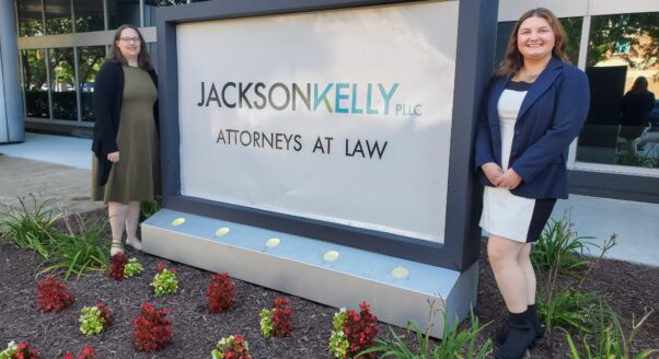 Volunteer Attorneys Angela and Jenna stand outside Jackson Kelly with the firm's sign.