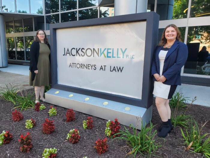 Volunteer Attorneys Angela and Jenna stand outside Jackson Kelly with the firm's sign.